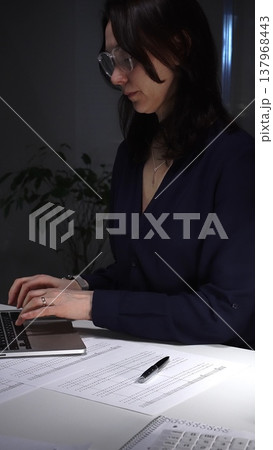 Woman's hands typing on laptop at office desk, working late night with calculator and financial documents. Audit and taxes in business 137968443