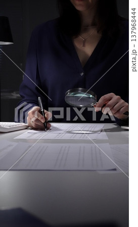Woman examining tax forms and financial statements at desk, using calculator and magnifying glass to verify figures and audit records. Audit and taxes theme in business Woman examining tax forms and financial statements at desk, using calculator and magnifying glass to verify figures and audit records. Audit and taxes theme in business 137968444