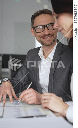 Business colleagues collaborating and discussing important company strategy and planning, a man explaining while a woman takes notes during a productive corporate meeting, vertical view 137968567
