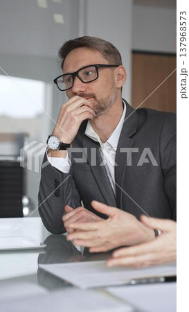 Business colleagues collaborating on an agreement, woman signing a document during a professional meeting in an office, man assisting her with information on a digital tablet, vertical view 137968573