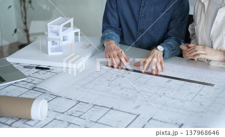 Architects working together, developing a building design by assembling a scale model and reviewing detailed blueprints, symbolizing teamwork, planning, and architectural creation Architects working together, developing a building design by assembling a scale model and reviewing detailed blueprints, symbolizing teamwork, planning, and architectural creation 137968646