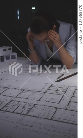 Architect woman experiencing stress and frustration from project deadline working late at night in office. Architecture and business concept in low key lighting Architect woman experiencing stress and frustration from project deadline working late at night in office. Architecture and business concept in low key lighting 137968770