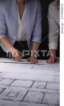 Architects and engineers collaborating on a building blueprint, measuring and discussing plans for a new construction project. Concept of architecture and business in low key lighting 137968833