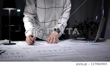 Business professional analyzing financial data and statistics. Working late night in a modern office. Using a laptop and reviewing documents with charts and graphs Business professional analyzing financial data and statistics. Working late night in a modern office. Using a laptop and reviewing documents with charts and graphs 137968903