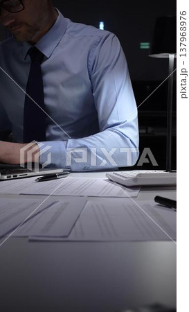 Businessman working meticulously with financial documents, using a pen and calculator to manage accounting tasks and reporting. Audit and taxes in business Businessman working meticulously with financial documents, using a pen and calculator to manage accounting tasks and reporting. Audit and taxes in business 137968976