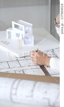 Female architect engrossed in architectural plans and miniature scale model, thoughtfully designing a new building project for modern construction development Female architect engrossed in architectural plans and miniature scale model, thoughtfully designing a new building project for modern construction development 137969028