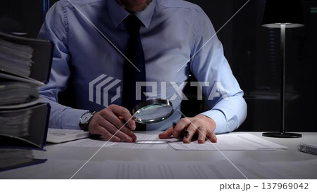 Financial auditor or accountant scrutinizing documents with a magnifying glass and calculator in a dark office. Audit and taxes in business Financial auditor or accountant scrutinizing documents with a magnifying glass and calculator in a dark office. Audit and taxes in business 137969042
