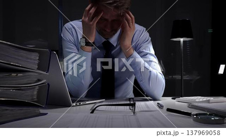 Stressed businessman suffering from headache and occupational burnout working late in a dark office. Audit and taxes in business 137969058