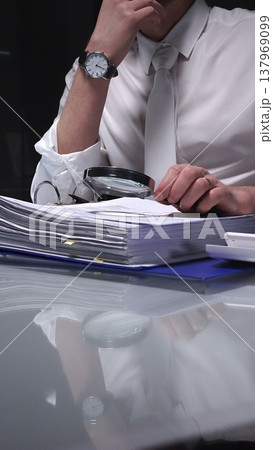 Businessman holding a magnifying glass and checking financial data, reviewing corporate audit reports, and analyzing various charts. Audit and taxes in business 137969099