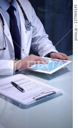 Medical doctor analyzing digital health records on a tablet computer, ensuring patient data management and secure care information in a modern clinic setting 137969145