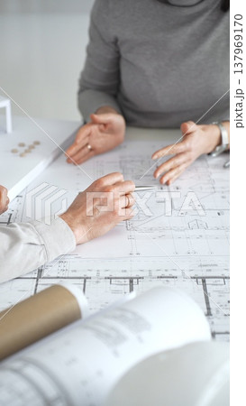 Architects discussing modern building design with 3d model and blueprints during planning meeting focused on innovation, teamwork and sustainable construction solutions, close up Architects discussing modern building design with 3d model and blueprints during planning meeting focused on innovation, teamwork and sustainable construction solutions, close up 137969170