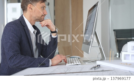 Man architect designing building plans on computer, thinking and concentrating on construction project blueprints at office desk. Business and architecture concept 137969177