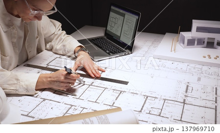 Architect carefully drawing blueprints for a new residential building project, refining floor plans on a laptop, working on a complex architectural design, close up 137969710