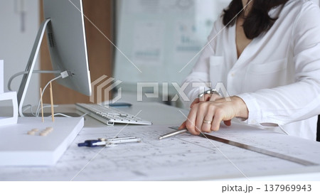 Architect drawing technical plans and working with scale models on a desk with a computer, focusing on design and engineering. Business and architecture concept 137969943