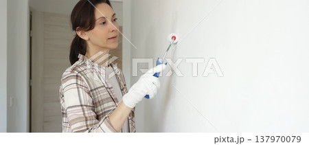 Woman wearing protective gloves painting white wall with small paint roller, updating interior and giving room clean, modern look during home renovation project Woman wearing protective gloves painting white wall with small paint roller, updating interior and giving room clean, modern look during home renovation project 137970079