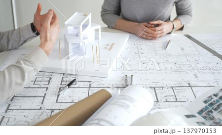 Architects discussing modern building design with 3d model and blueprints during planning meeting focused on innovation, teamwork and sustainable construction solutions, close up Architects discussing modern building design with 3d model and blueprints during planning meeting focused on innovation, teamwork and sustainable construction solutions, close up 137970153