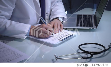 Stethoscope laying on a white reflective desk while doctor man working in clinic office. Typing on laptop and writing notes. Medicine concept 137970186
