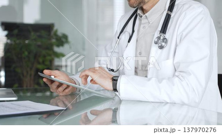Doctor man in white coat using tablet, working with patient medical records and digital health information in clinic. Medicine, healthcare and science concept Doctor man in white coat using tablet, working with patient medical records and digital health information in clinic. Medicine, healthcare and science concept 137970276