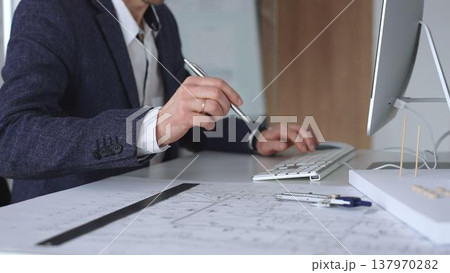 Architect hand drawing on building blueprints, creating an architectural model, and using a computer for project design. Business and architecture concept 137970282