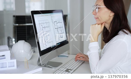 Woman architect analyzing construction blueprint on computer screen in modern design office, planning new building project. Business and architecture concept 137970356