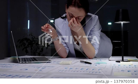 Stressed business woman suffering from headache in dark office, hands on head experiencing burnout and fatigue during late night work, facing deadline pressure and financial difficulties 137970358