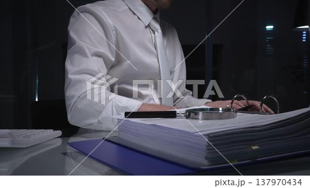 Businessman analyzing financial documents and paperwork at desk, working overtime in a dark office, researching data for investigation. Audit and taxes in business Businessman analyzing financial documents and paperwork at desk, working overtime in a dark office, researching data for investigation. Audit and taxes in business 137970434