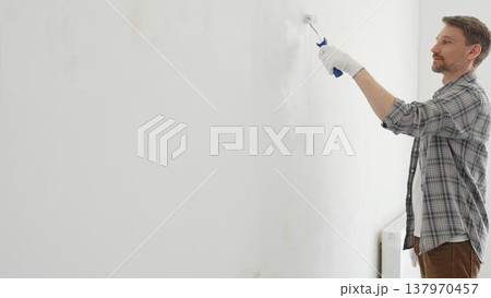 Professional house painter applying white paint to an interior wall with a roller during home renovation. Focus on the skilled hand maneuvering the tool for a fresh, clean finish Professional house painter applying white paint to an interior wall with a roller during home renovation. Focus on the skilled hand maneuvering the tool for a fresh, clean finish 137970457