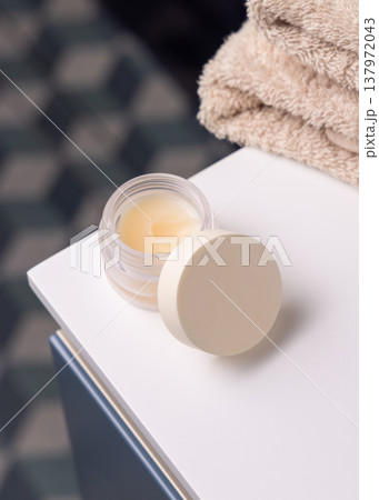 Opened handmade lip balm jar in blue bathroom with towel. Blank lid cosmetic mockup Opened handmade lip balm jar in blue bathroom with towel. Blank lid cosmetic mockup 137972043