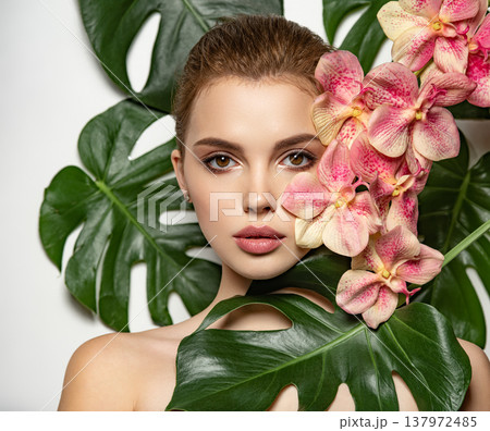 Pretty girl in Skin care beauty treatments concept. Beautiful woman with green leave near face and body. Closeup girl's face with green leave. Model with pink tropical orchid near face. Brown Pretty girl in Skin care beauty treatments concept. Beautiful woman with green leave near face and body. Closeup girl's face with green leave. Model with pink tropical orchid near face. Brown 137972485