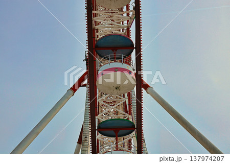Low Angle View of Ferris Wheel Cabins and Steel Framework, Symmetrical Architectural Perspective of Amusement Ride, Modern Entertainment Structure Against Pale Blue Sky, Urban Park Low Angle View of Ferris Wheel Cabins and Steel Framework, Symmetrical Architectural Perspective of Amusement Ride, Modern Entertainment Structure Against Pale Blue Sky, Urban Park 137974207