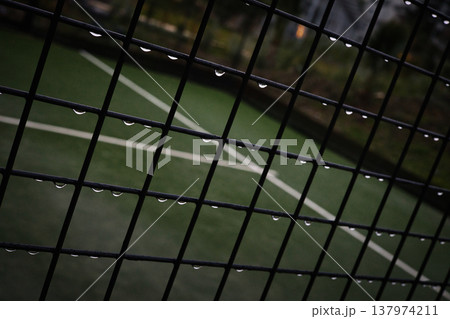 Close-up of Metal Fence with Raindrops on Green Sports Field Background, Abstract Grid Pattern with Water Droplets, Outdoor Tennis Court or Football Pitch during Rainy Weather Details Close-up of Metal Fence with Raindrops on Green Sports Field Background, Abstract Grid Pattern with Water Droplets, Outdoor Tennis Court or Football Pitch during Rainy Weather Details 137974211