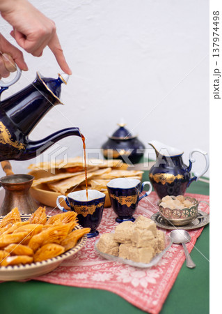 Hand pours tea from a cobalt blue vintage teapot in cups. Traditional oriental sweets baklava and halva. Sweet food 137974498