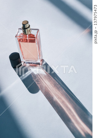 Fragrance bottle with pink liquid creating long, artistic shadow on clear background 137975473