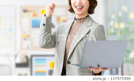 パソコンを持ってガッツポーズをする女性・ビジネスウーマン 137975990