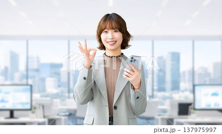 スマートフォンを持ってOKポーズをする笑顔の女性・ビジネスウーマン スマートフォンを持ってOKポーズをする笑顔の女性・ビジネスウーマン 137975997