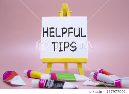 Helpful tips symbol. Wooden blocks with words Helpful tips. Beautiful pink background with paints and easel. Business and Helpful tips concept. Copy space. 137977001
