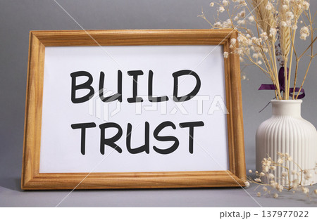 Build trust symbol. Concept words Build trust on beautiful wooden picture frame. Beautiful grey background with flower vase. Business and Build trust concept. Copy space. Build trust symbol. Concept words Build trust on beautiful wooden picture frame. Beautiful grey background with flower vase. Business and Build trust concept. Copy space. 137977022