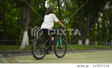 Woman riding bicycle in park rear view 4k Woman riding bicycle in park rear view 4k 137977179