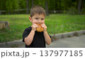 Little boy eats cheeseburger in park and looks at camera portrait shot 4k 137977185