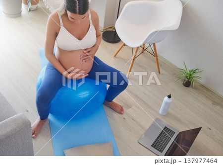 Pregnant woman exercising on a fitness ball at home 137977464