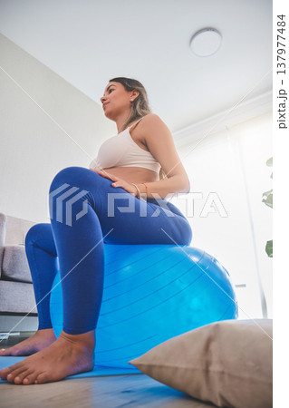 Pregnant woman exercising at home using stability ball Pregnant woman exercising at home using stability ball 137977484