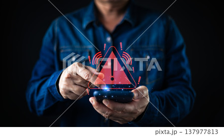 A person using a smartphone triggers a glowing red warning alert icon with an exclamation mark, symbolizing cybersecurity risks, data breaches, system errors, and mobile security threats. A person using a smartphone triggers a glowing red warning alert icon with an exclamation mark, symbolizing cybersecurity risks, data breaches, system errors, and mobile security threats. 137977813
