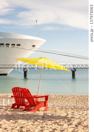 Close-up of beach chair and colourful napkins on the sand of a Bahamian beach. A cruise ship at anchor in the background Tourism and holiday concept Close-up of beach chair and colourful napkins on the sand of a Bahamian beach. A cruise ship at anchor in the background Tourism and holiday concept 137978063