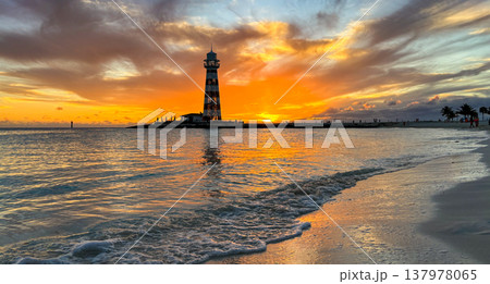 The sun dips into the horizon behind the clouds, on a Bahamian island at sunset.Backlit lighthouse.Banner for tourist or travel promotion. 137978065