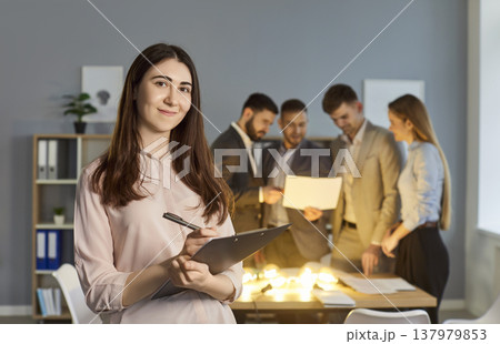 Portrait of smiling young businesswoman with professional team brainstorming on ideas in background. 137979853