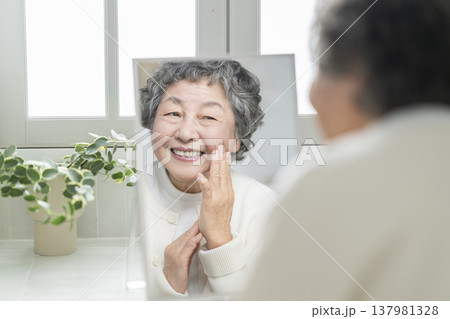 鏡を見ながら頬に手をあてて微笑む80代の女性　スキンケア・ビューティ　イメージ 137981328