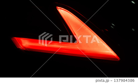 Abstract and showcasing the sleek design of a modern car LED taillight. In the darkness. Intricate red lighting elements and clear lens highlight advanced automotive lighting technology. Abstract and showcasing the sleek design of a modern car LED taillight. In the darkness. Intricate red lighting elements and clear lens highlight advanced automotive lighting technology. 137984386