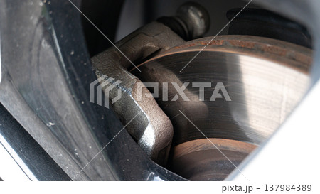 Detailed close up of a vehicle's disc brake system. Featuring a worn metal rotor and brake caliper assembly. Highlights the mechanical components behind the wheel. Detailed close up of a vehicle's disc brake system. Featuring a worn metal rotor and brake caliper assembly. Highlights the mechanical components behind the wheel. 137984389