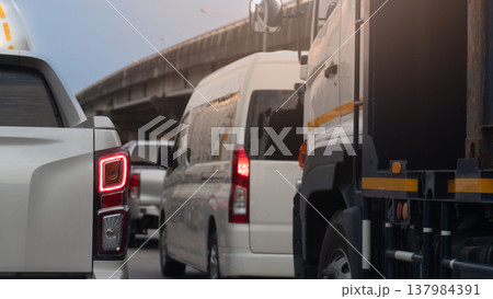 Rear side of pikup white car with turn on brake light. Traffic jam on the road with many car. Concrete overpass bridge on the side of the road. Under clear blue sky. 137984391