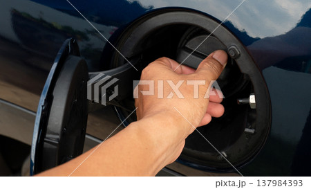Close up shot of a black plastic fuel gas cap with a ridged edge for easy gripping. Handle to twist the fuel filler cap open or close. A luxurious dark blue car. 137984393